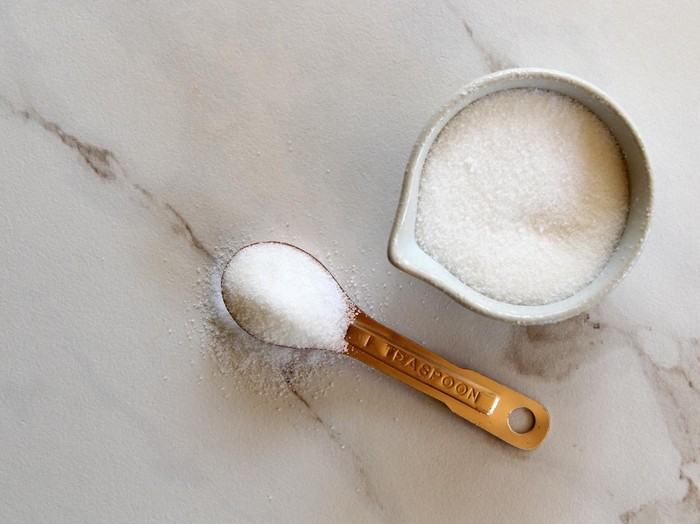 Sugar on a copper teaspoon and a cup of sugar. White marble copy space.