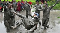 Para petani riang gembira bermain lumpur di sawah, sambil sesekali melempar rekannya ke kubangan lumpur.