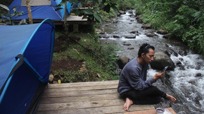 Pengunjung bersantai sambil menikmati suasana alam di samping tenda tempat wisata Kebon Pitu, Dusun Dampak, Desa Panglungan, Kecamatan Wonosalam, Kabupaten Jombang, Jawa Timur, Sabtu (2/7/2022). Destinasi wisata Kebon Pitu Wonosalam menyediakan tujuh tenda menghadap ke aliran sungai dari Pegunungan Anjasmoro dengan biaya sewa per malam Rp400 ribu saat akhir pekan dan Rp350 ribu pada hari biasa. ANTARA FOTO/Syaiful Arif/rwa.