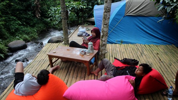 Pengunjung bersantai sambil menikmati suasana alam di samping tenda tempat wisata Kebon Pitu, Dusun Dampak, Desa Panglungan, Kecamatan Wonosalam, Kabupaten Jombang, Jawa Timur, Sabtu (2/7/2022).