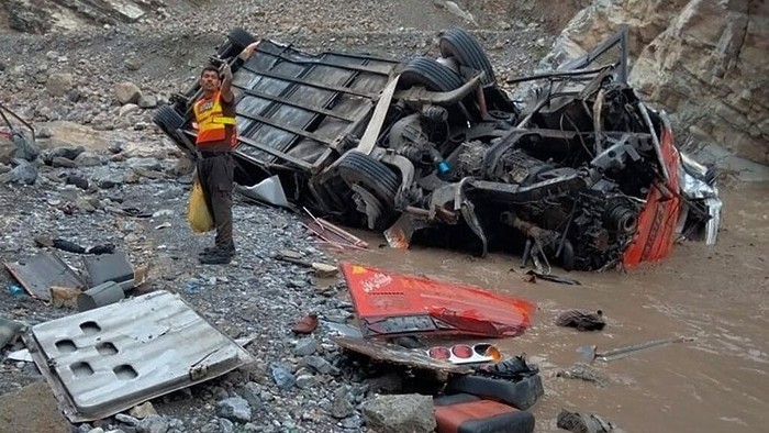 In this photo provided by Baluchistans rescue department, a rescue worker stands next to the wreck of a passenger bus, in Zhob, Baluchistan province, in southwest Pakistan, Sunday, July 3, 2022. An official said the passenger bus slid off a mountain road and fell 200 feet (61 meters) into a ravine in heavy rain killing at least 18 people and injuring some 12 others. (Baluchistan Rescue Department via AP)