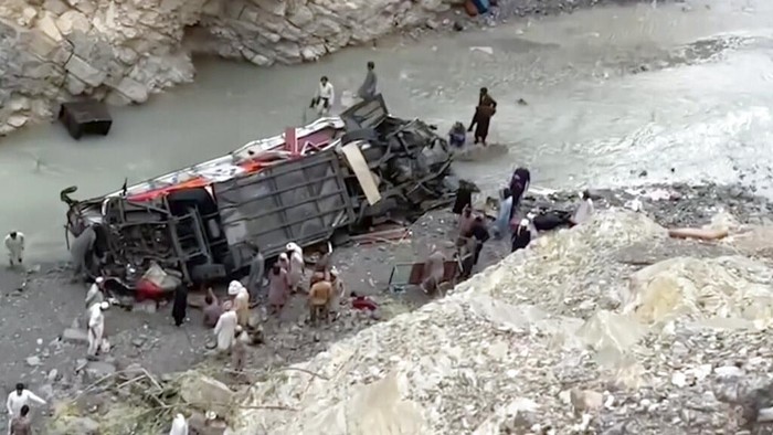 In this photo provided by Baluchistan's rescue department, a rescue worker stands next to the wreck of a passenger bus, in Zhob, Baluchistan province, in southwest Pakistan, Sunday, July 3, 2022. An official said the passenger bus slid off a mountain road and fell 200 feet (61 meters) into a ravine in heavy rain killing at least 18 people and injuring some 12 others. (Baluchistan Rescue Department via AP)