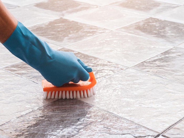 Hand of man wearing blue rubber gloves is used to convert scrub cleaning on the tile floor.
