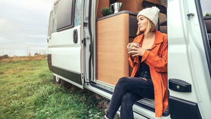 Woman drinking coffee sitting at the door of a camper van