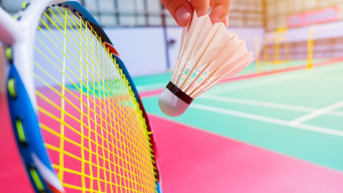 Bulu Tangkis close up hand hold serve badminton shuttlecock with blur badminton court background