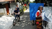 Pesepeda melintas di samping petugas yang sedang memegang background untuk foto eKTP warga. 