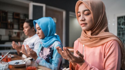 Hijab women and a man pray together before meals, a fast breaking meal served on a table in backyard