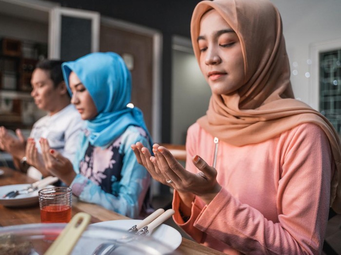 Hijab women and a man pray together before meals, a fast breaking meal served on a table in backyard