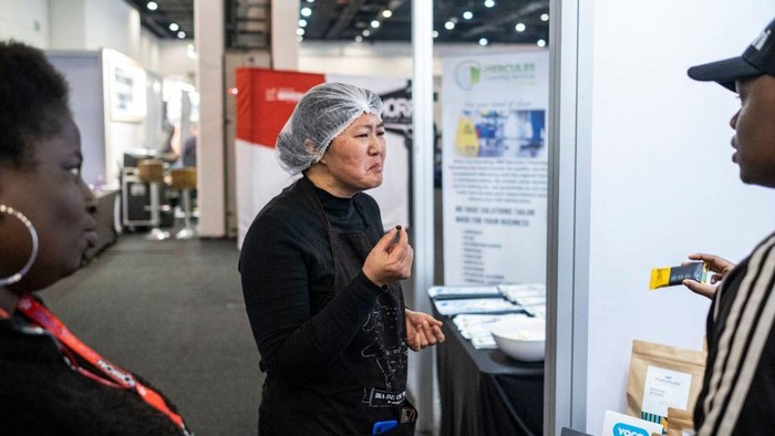 A vendor (L) interacts with attendees as they taste mopani worm chocolate at the Hostex food Expo in Sandton on June 27, 2022. - A South African start-up entrepreneur is changing the way people view and eat protein- and iron-packed mopane caterpillars.
For the past seven months Wendy Vesela has been cooking up a culinary buzz selling iron-packed insects caterpillars known as mopane worms in wafer-like biscuits, energy bars, or as a pizza topping.
The 40-year-old chemical engineer found creative ways to serve the spiky black and green caterpillars that some people find gross.
She is selling them at home and abroad in trendy packaging as dried whole mopanes, but also as a milled flour that can be substituted for protein powder as well as a savory biscuit and sweet chocolate protein bar. (Photo by EMMANUEL CROSET / AFP) (Photo by EMMANUEL CROSET/AFP via Getty Images)