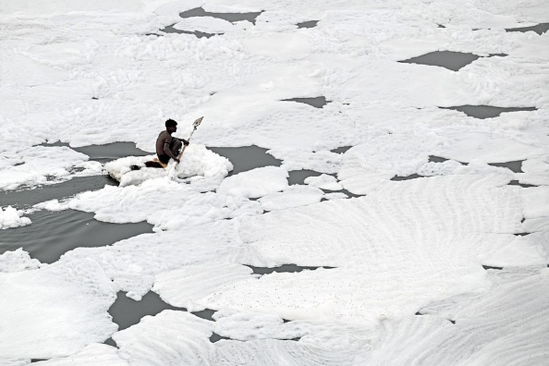 A man paddles his raft while collecting recyclable materials in the waters of river Yamuna coated with polluted foam in New Delhi on July 5, 2022. (Photo by Sajjad HUSSAIN / AFP) (Photo by SAJJAD HUSSAIN/AFP via Getty Images)