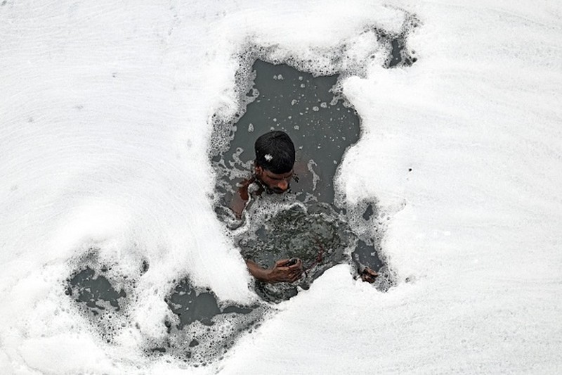 A man paddles his raft while collecting recyclable materials in the waters of river Yamuna coated with polluted foam in New Delhi on July 5, 2022. (Photo by Sajjad HUSSAIN / AFP) (Photo by SAJJAD HUSSAIN/AFP via Getty Images)
