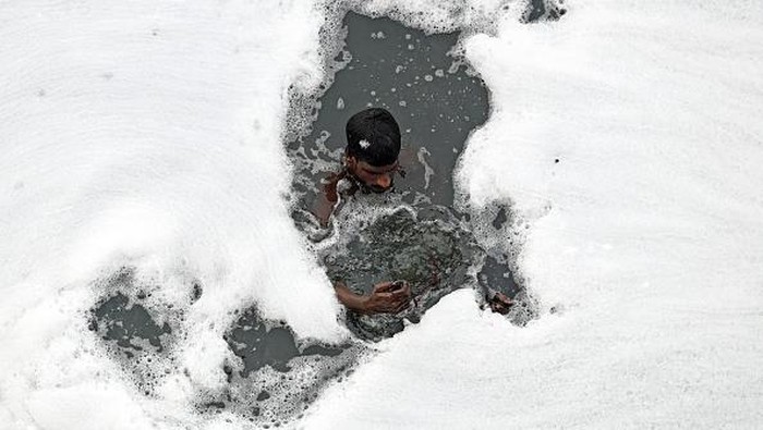 A man paddles his raft while collecting recyclable materials in the waters of river Yamuna coated with polluted foam in New Delhi on July 5, 2022. (Photo by Sajjad HUSSAIN / AFP) (Photo by SAJJAD HUSSAIN/AFP via Getty Images)