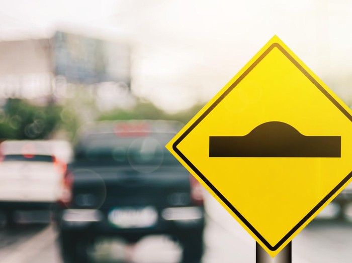 Hump warning sign on blur traffic road with colorful bokeh light abstract background. Copy space of transportation and travel concept. Retro tone filter effect color style.
