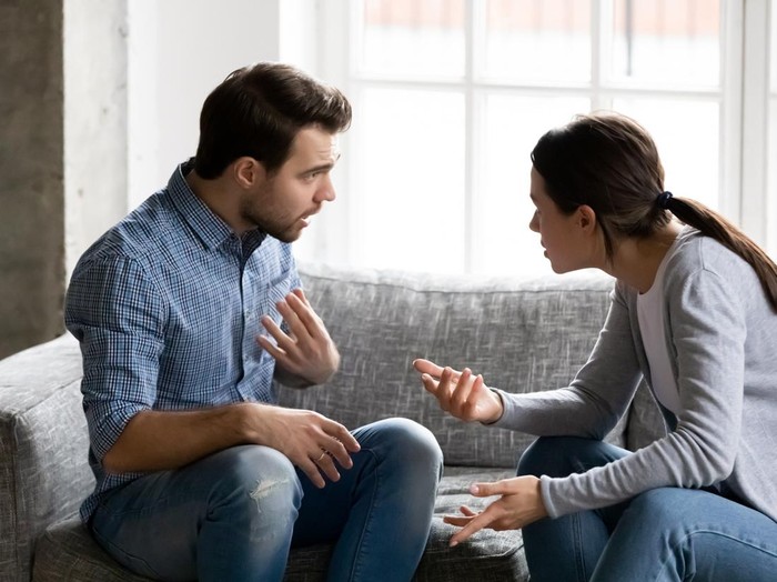 Stressed young married family couple arguing emotionally, blaming lecturing each other, sitting on couch. Depressed husband quarreling with wife, having serious relations communication problems.