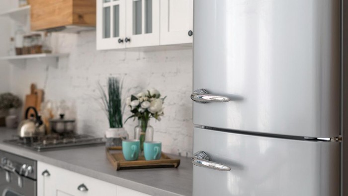 Selective focus on new refrigerator against wooden furniture with cabinets in modern kitchen. Concept of apartment with white interior