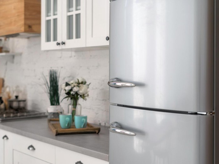 Selective focus on new refrigerator against wooden furniture with cabinets in modern kitchen. Concept of apartment with white interior