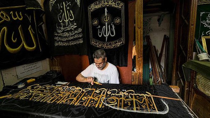 An embroiderer sews with gold thread a verse from the Holy Koran, Islam's holy book, onto a replica of the Kiswa, the cloth used to cover the Kaaba at the Grand Mosque in the Muslim holy city of Mecca, to be sold as a souvenir for tourists visiting the historic district of al-Hussein of Islamic Cairo in Egypt's capital on June 15, 2022. - From the 13th century, Egyptian artisans made the giant cloth in sections, which authorities transported to Mecca with great ceremony. Celebrations would mark processions through cities, flanked by guards and clergymen as Egyptians sprinkled rosewater from balconies above. From 1927, manufacturing began to move to Mecca in the nascent Kingdom of Saudi Arabia, which would fully take over production of the kiswa in 1962. (Photo by Khaled DESOUKI / AFP) (Photo by KHALED DESOUKI/AFP via Getty Images)