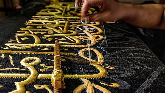 Lihat Lebih Dekat Pembuatan Kiswah Ka'bah di Mesir An embroiderer sews with gold thread a verse from the Holy Koran, Islam's holy book, onto a replica of the Kiswa, the cloth used to cover the Kaaba at the Grand Mosque in the Muslim holy city of Mecca, to be sold as a souvenir for tourists visiting the historic district of al-Hussein of Islamic Cairo in Egypt's capital on June 15, 2022. - From the 13th century, Egyptian artisans made the giant cloth in sections, which authorities transported to Mecca with great ceremony. Celebrations would mark processions through cities, flanked by guards and clergymen as Egyptians sprinkled rosewater from balconies above. From 1927, manufacturing began to move to Mecca in the nascent Kingdom of Saudi Arabia, which would fully take over production of the kiswa in 1962. (Photo by Khaled DESOUKI / AFP) (Photo by KHALED DESOUKI/AFP via Getty Images)