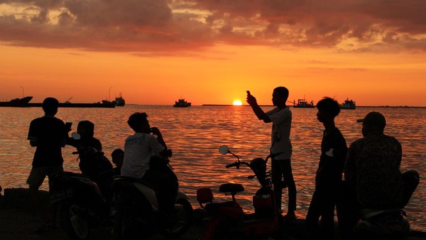Sejumlah remaja menikmati suasana matahari terbenam (sunset) di Pelabuhan Rakyat Paotere, Makassar, Sulawesi Selatan, Selasa (5/7/2022).   