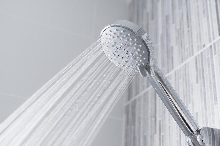 Fresh shower behind wet glass window with water drops splashing. Water running from shower head and faucet in modern bathroom.