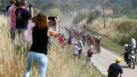 Pebalap melintasi jalan berbatu di tengah pedesaan di antara ladang gandum siap panen. Debu dan jalan bergelombang menjadi santapan wajib pembalap.  (Tim de Waele/Getty Images)