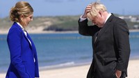 PM Boris Johnson memegang rambutnya yang terkena angin pantai di depan istrinya, Carrie saat tiba dalam pertemuan G7 di Cornwall, Inggris, 12 Juni 2021. Boris Johnson dilaporkan akan mengundurkan diri sebagai pemimpin Partai Konservatif yang kini berkuasa di negara tersebut. Kendati demikian, Boris Johnson akan tetap menjabat sebagai PM hingga pemimpin baru terpilih pada musim gugur nanti. (AP Photo/Kirsty Wigglesworth) 