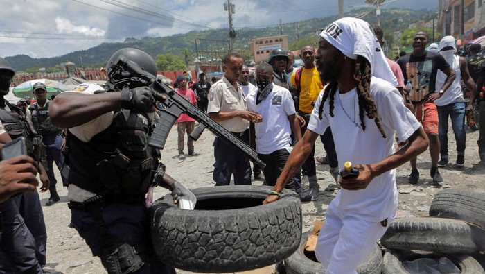 Aksi Ricuh Warnai Peringatan Satu Tahun Pembunuhan Presiden Haiti Moise A police officer holding a gun confronts a demonstrator over setting a roadblock with a tire during a protest to demand justice for President Jovenel Moise a year after his assassination, in Port-au-Prince, Haiti July 7, 2022. REUTERS/Ralph Tedy Erol TPX IMAGES OF THE DAY
