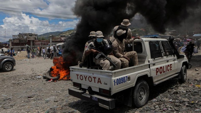 Aksi Ricuh Warnai Peringatan Satu Tahun Pembunuhan Presiden Haiti Moise A police officer holding a gun confronts a demonstrator over setting a roadblock with a tire during a protest to demand justice for President Jovenel Moise a year after his assassination, in Port-au-Prince, Haiti July 7, 2022. REUTERS/Ralph Tedy Erol TPX IMAGES OF THE DAY