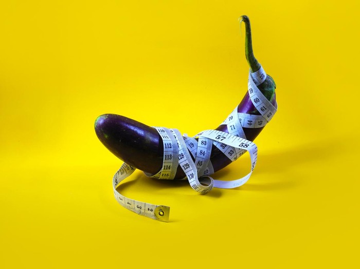 Close-up view of Purple eggplant wrapped with white measuring tape isolated on a yellow background. Concept of an increasing penis in men, viagra