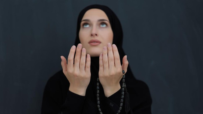 Portrait of young Muslim woman making dua. Arabian girl wearing abaya keeps hands in praying gesture. Representing worship to God and Ramadan Kareem concept