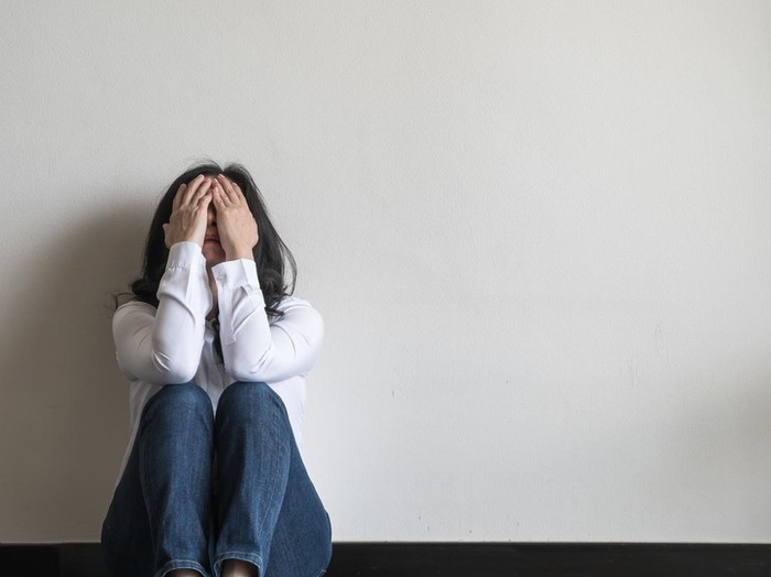 Anxiety disorder menopause woman, stressful depressed emotional person with mental health illness, headache and migraine sitting feeling bad sadly with back against wall on the floor in domestic home
