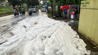 Nampak busa hampir memenuhi jalan, tebalnya busa membuat pemilik rumah menyiram busa dengan air.
