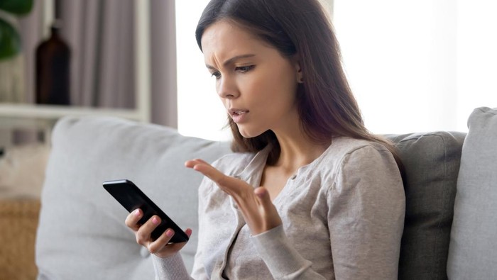 Woman sit on sofa holding smartphone cover face with hand feels scared humiliated suffering from cyberbullying being on-line abused by stalker. Bad news, life troubles, break up with boyfriend concept