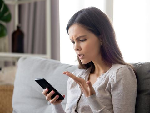 1251273723 Woman sit on sofa holding smartphone cover face with hand feels scared humiliated suffering from cyberbullying being on-line abused by stalker. Bad news, life troubles, break up with boyfriend concept