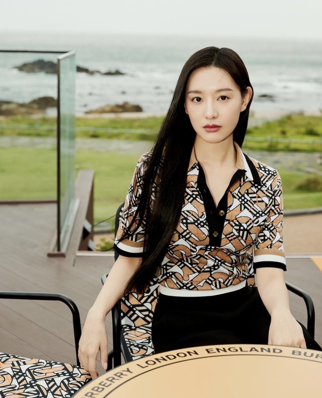Berlatar pemandangan pantai, Kim Ji Won terlihat elegan memakai Monogram Wool Blend Jacquard Polo Shirt. Dia tak perlu memakai aksesori untuk terlihat stunning. Foto: dok. Burberry