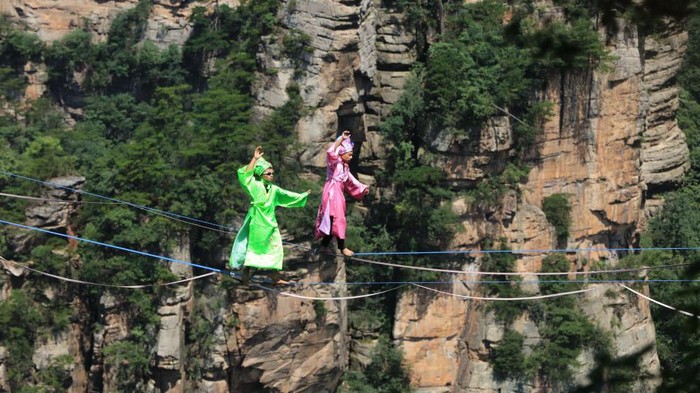 1407975696 ZHANGJIAJIE, CHINA - JULY 10: Slackline walkers in traditional Chinese costumes compete during a high-altitude slackline competition at Zhangjiajie National Forest Park on July 10, 2022 in Zhangjiajie, Hunan Province of China. (Photo by VCG/VCG via Getty Images)