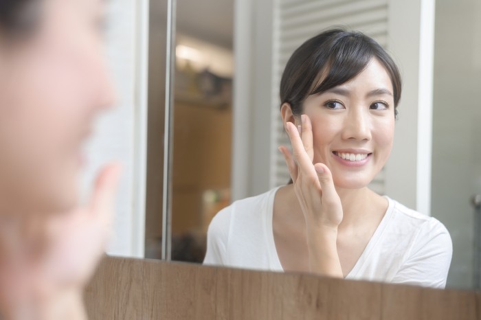 Ilustrasi Kandungan Skincare A happy beautiful woman applying moisturizing cream on face, skin care and treatment concept
