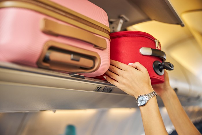 Arms shoving a small piece of luggage to the top shelf of an aircraft.