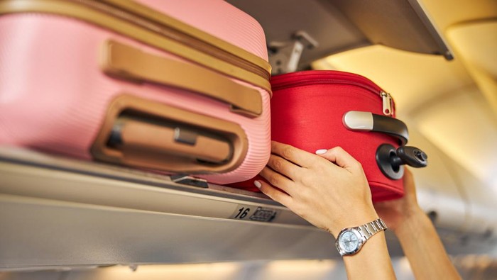 Arms shoving a small piece of luggage to the top shelf of an aircraft.