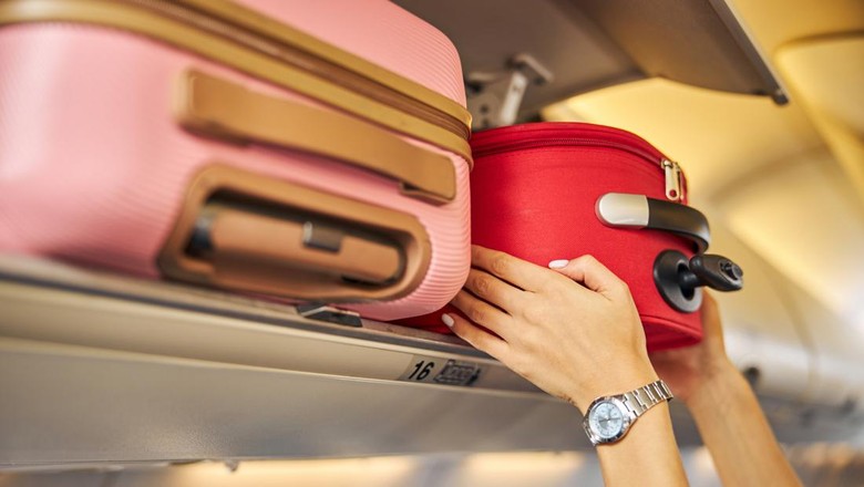 1281875469 Arms shoving a small piece of luggage to the top shelf of an aircraft.