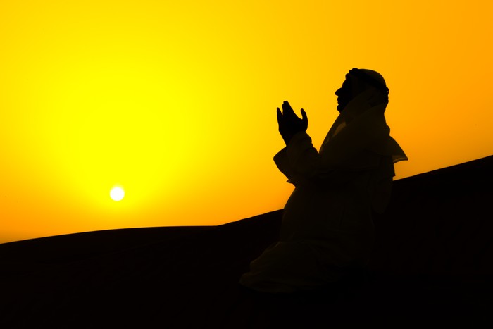 An Arab man is praying over sand dunes of Dubai, United Arab Emirates