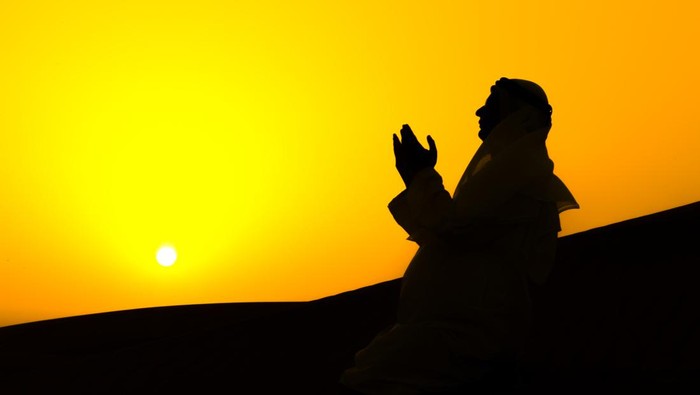 An Arab man is praying over sand dunes of Dubai, United Arab Emirates