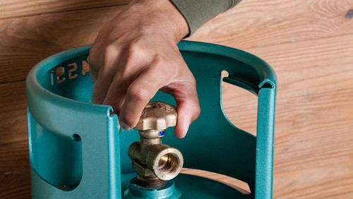 Closeup mans hand operating valve of LPG cylinder for cooking