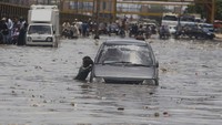 Seorang anak mencari rezeki dengan menawarkan jasa mendorong mobil yang mogok akibat banjir.