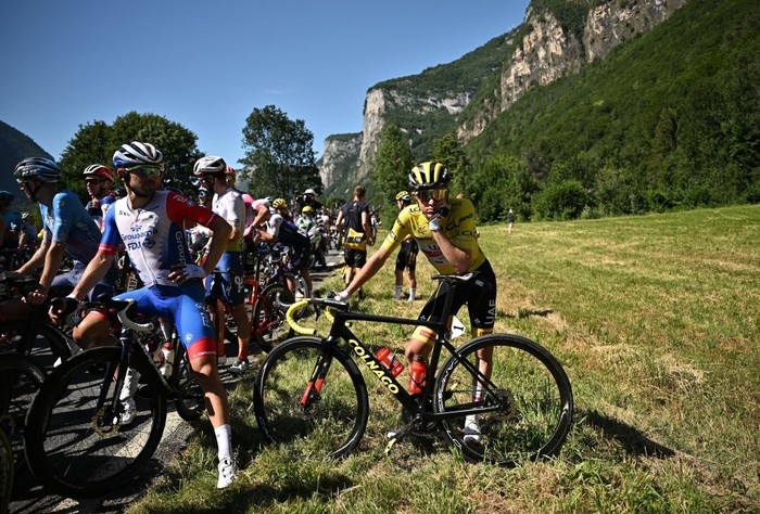 1241857527 UAE Team Emirates team's Slovenian rider Tadej Pogacar (C) wearing the overall leader's yellow jersey and the pack of riders are temporarily immobilized by race regulators due to a demonstration by environmental protestors on the race route during the 10th stage of the 109th edition of the Tour de France cycling race, 148,1 km between Morzine and Megeve, in the French Alps, on July 12, 2022. (Photo by Marco BERTORELLO / AFP) (Photo by MARCO BERTORELLO/AFP via Getty Images)
