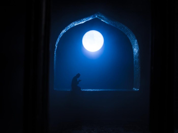 A realistic Arabian interior miniature with window and columns. Silhouette of muslim praying on carpet near window. Festive greeting card, invitation for Muslim holy month Ramadan Kareem. Selective focus