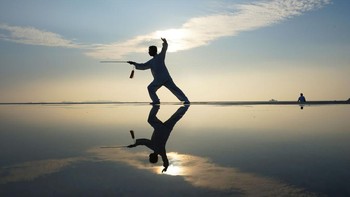 Seorang warga Yantai, China, yang berlatih pedang dengan teknik Tai Chi ini dimanfaatkan fotografer untuk mengambil jepretan refleksi dipadu dengan siluet. Hasilnya bikin pangling.
