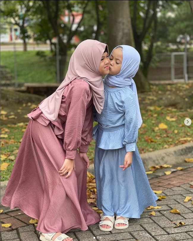 Aleena berpose sedang dicium pipinya oleh sang adik. I love you adreena 🤍🤍m tulis akun Instagram @aleenaaufar. Keduanya terlihat kompak memakai hijab dan dress dengan modelnya sama, namun berbeda warna. Foto: Dok. Instagram @aleenaaufar.