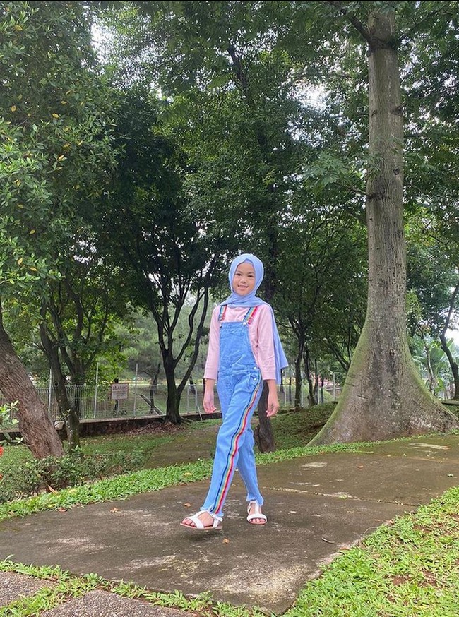 Aleena berpose OOTD di taman dengan mengenakan hijab pashmina bahan kaus warna biru. Gaya hijab Aleena serupa dengan sang ibu yang sehari-hari pakai hijab pashmina. Alenna memakai overall jeans. Foto: Dok. Instagram @aleenaaufar.
