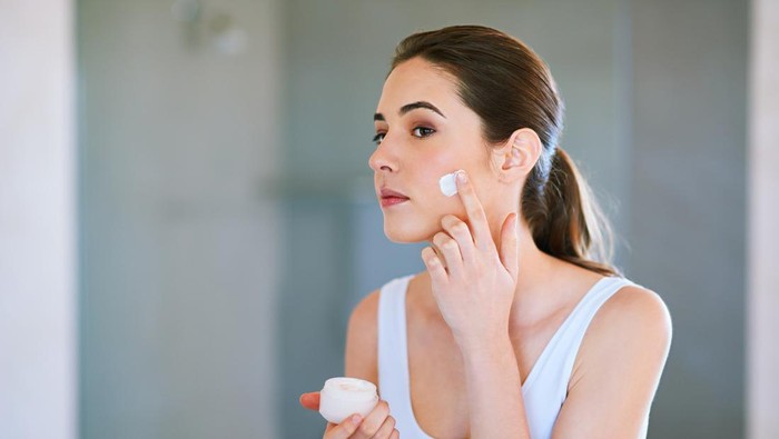 An attractive young woman applying cream to her face